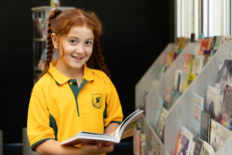 A youg girl reading a book in the library.