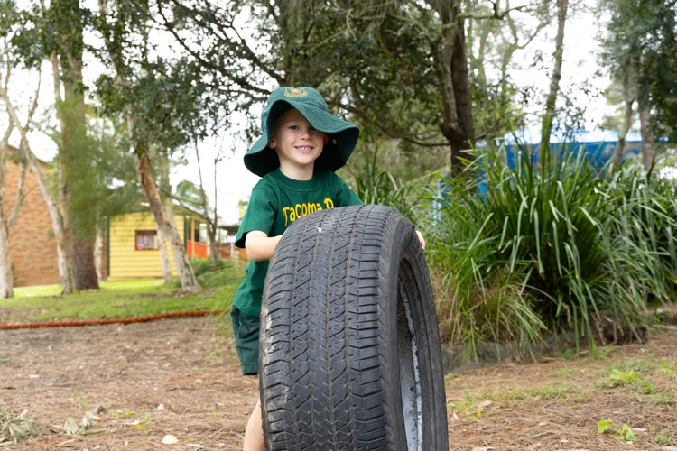 A young boy rolling a tyre in the playground.