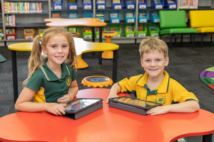 Two young students with iPads in the library.